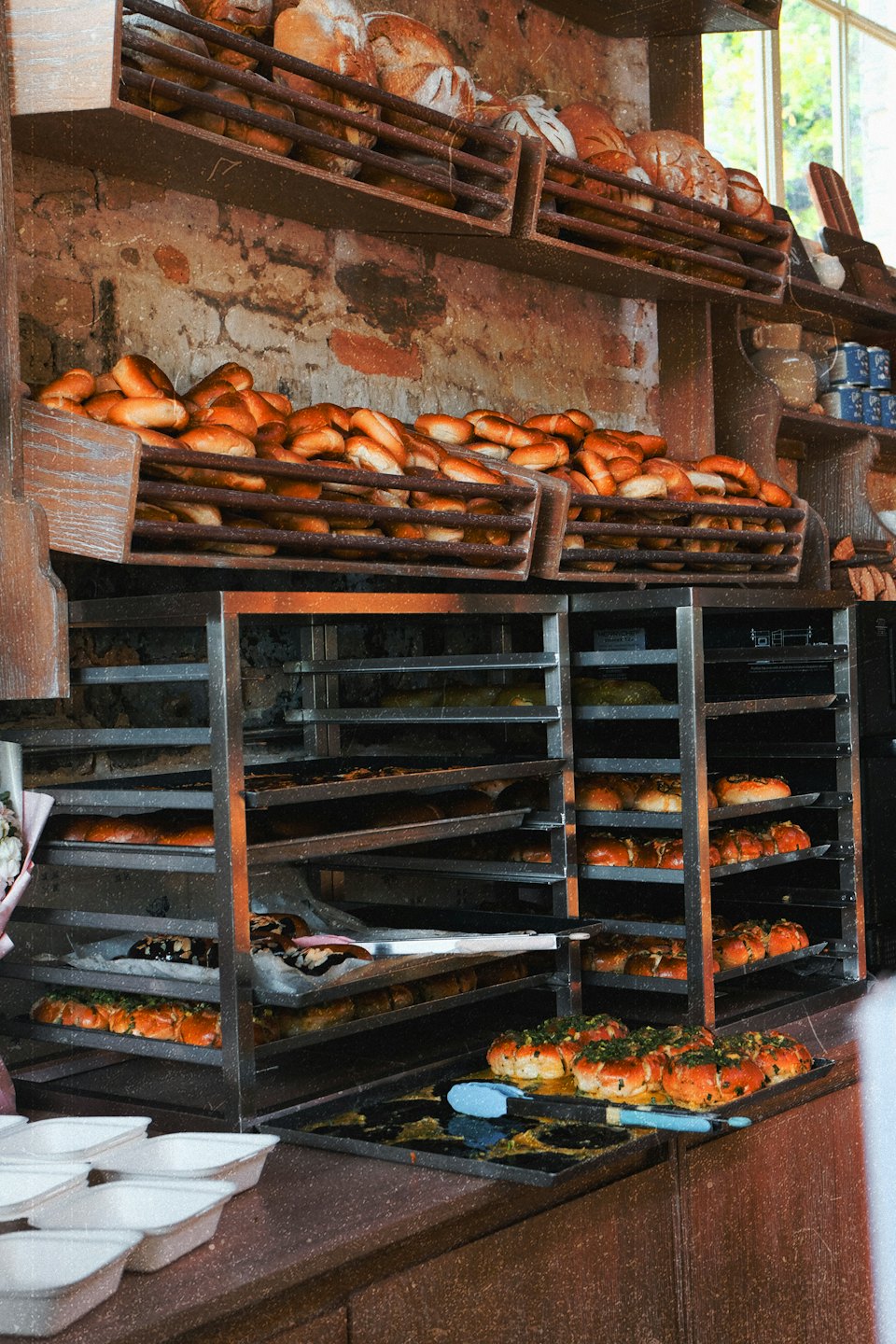 Frische Brote und Brötchen stehen in einem Holzregal in einer Bäckerei.